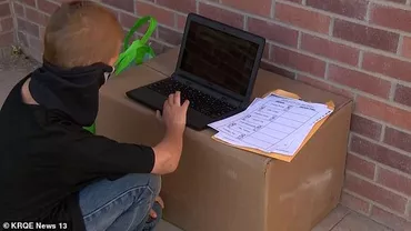 Un băiețel își face temele pe trotuarul din fața școlii închise. Copilul e prea sărac și nu are bani pentru internet acasă (GALERIE FOTO)